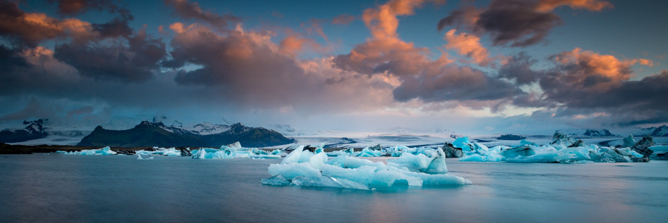 The sunrise colors in the clouds and mountains in the background provide context to the icebergs.